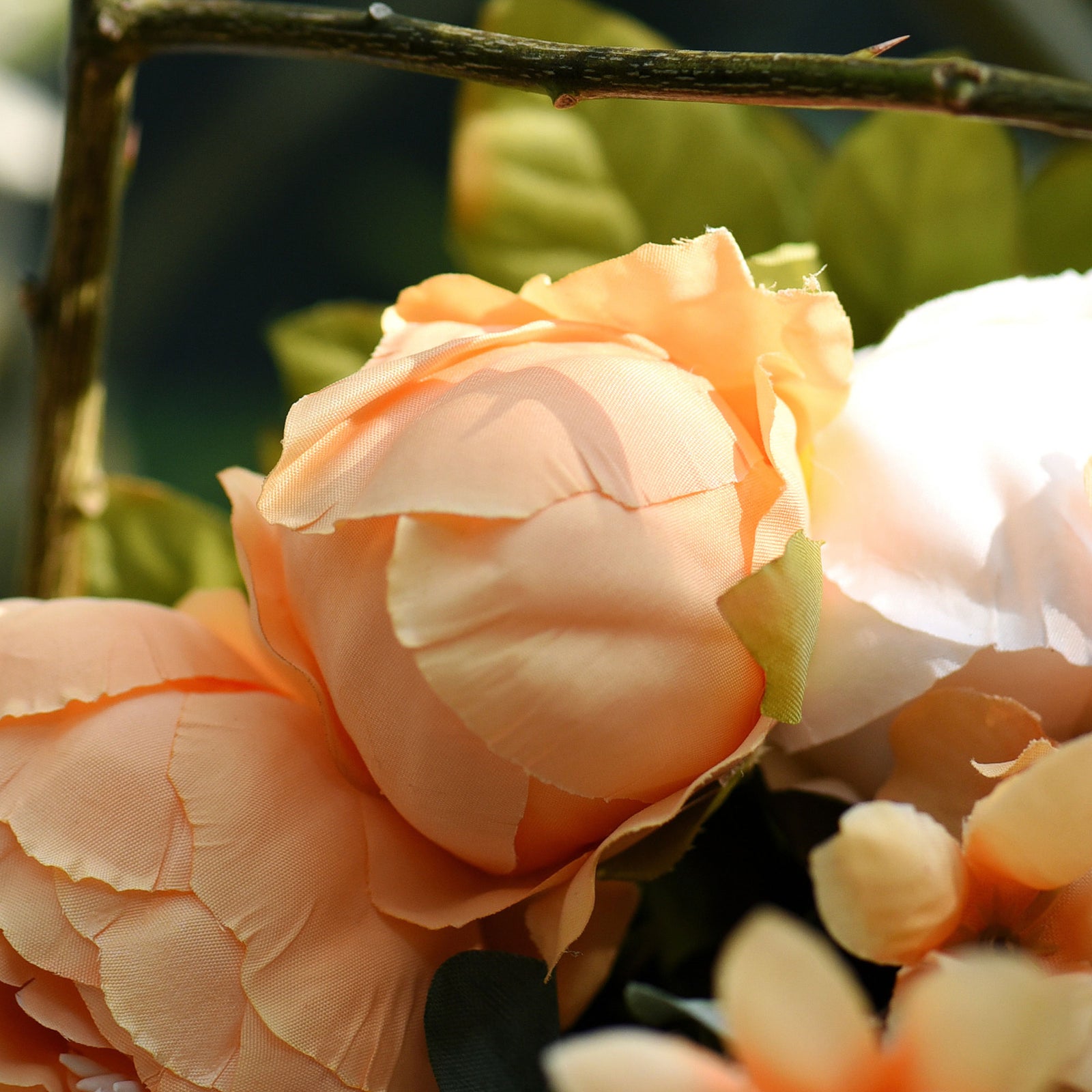 A close-up of artificial cream and peach peony flowers with soft petals and green leaves for a natural look.