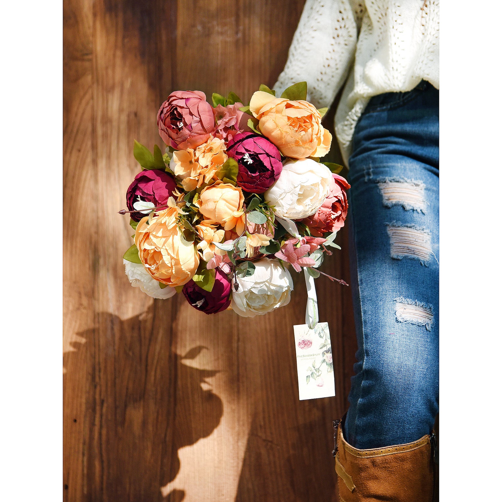 A person holding a mixed artificial peony bouquet in cream, peach, and burgundy colors, perfect for weddings or events.