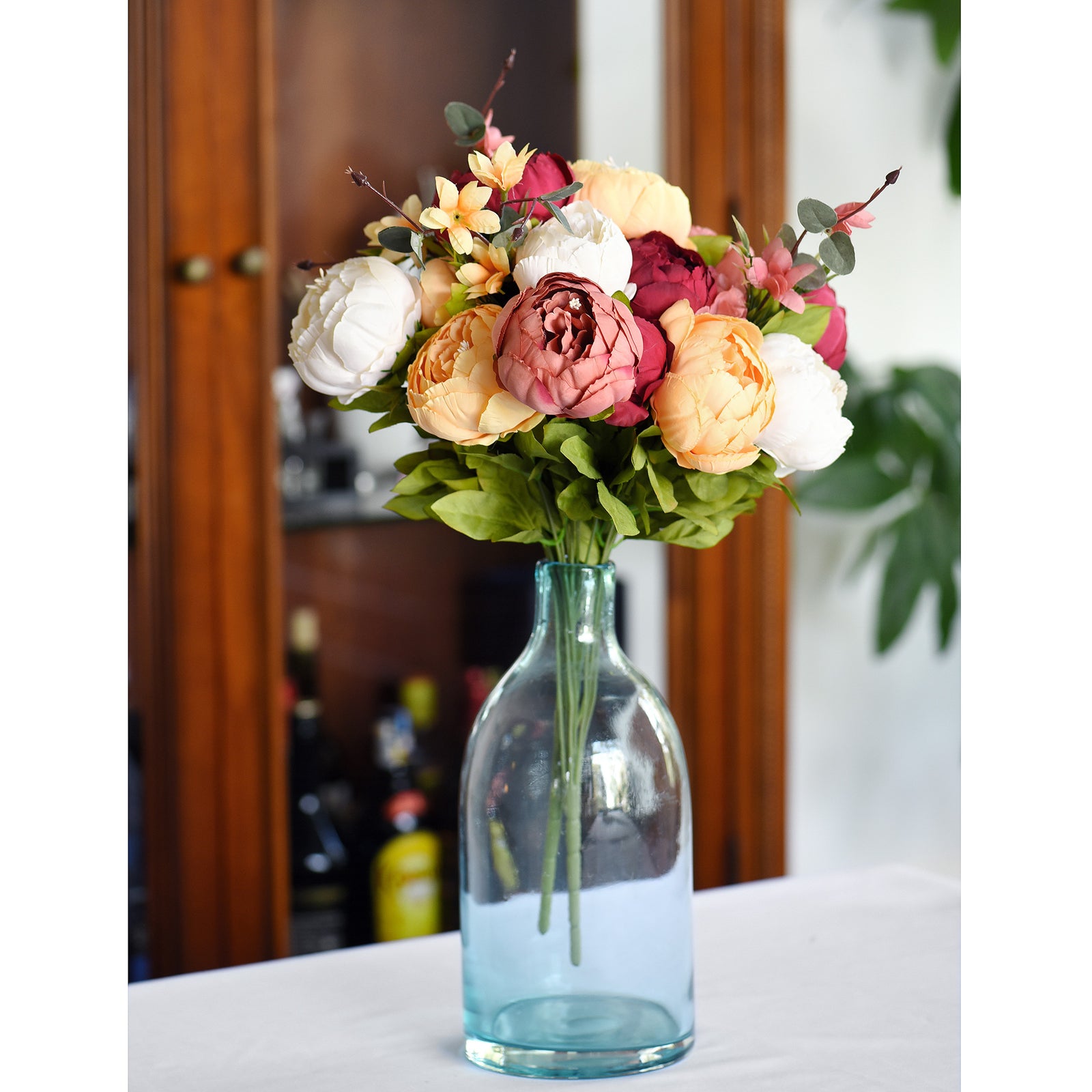 A delicate arrangement of mixed artificial peonies in a clear glass vase, displayed on a table for home decor.