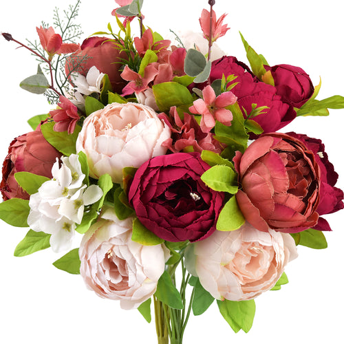 A vibrant artificial peony bouquet featuring lush silk flowers in shades of blush pink, deep burgundy, and warm coral, accented with greenery and small blossoms.