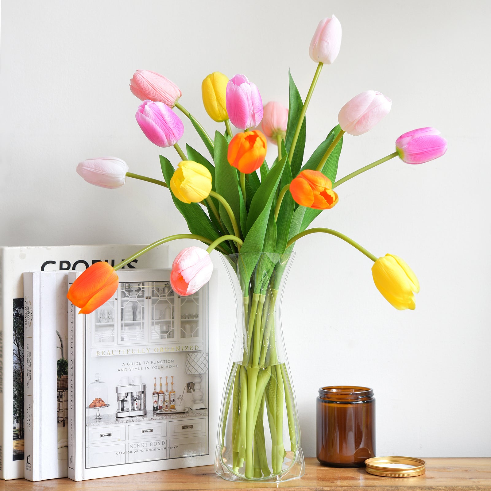 Bright artificial tulip arrangement on a desk with books and decor accents, showcasing vibrant spring colors.
