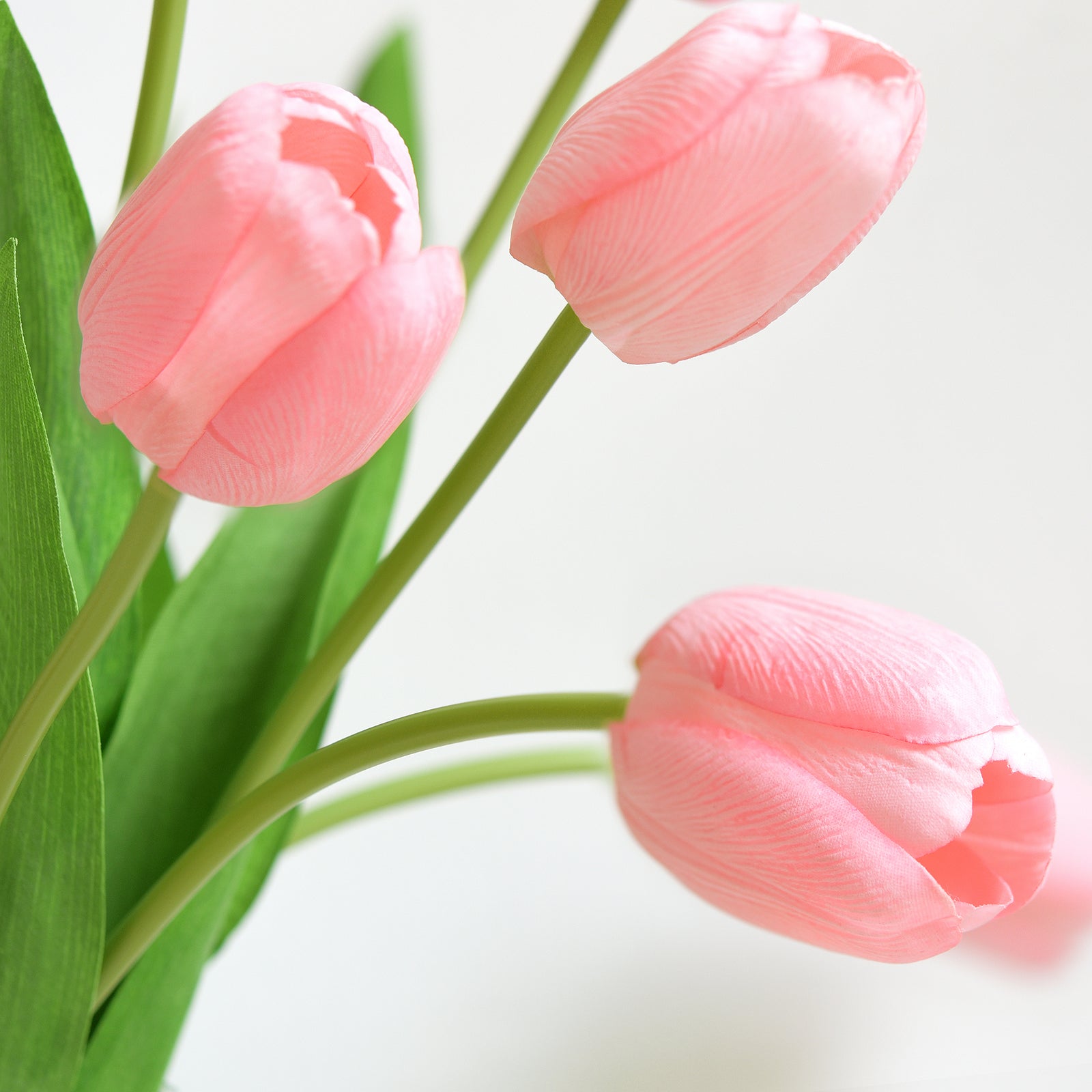 Close-up of lifelike blush pink artificial tulip petals with realistic texture and vibrant green stems