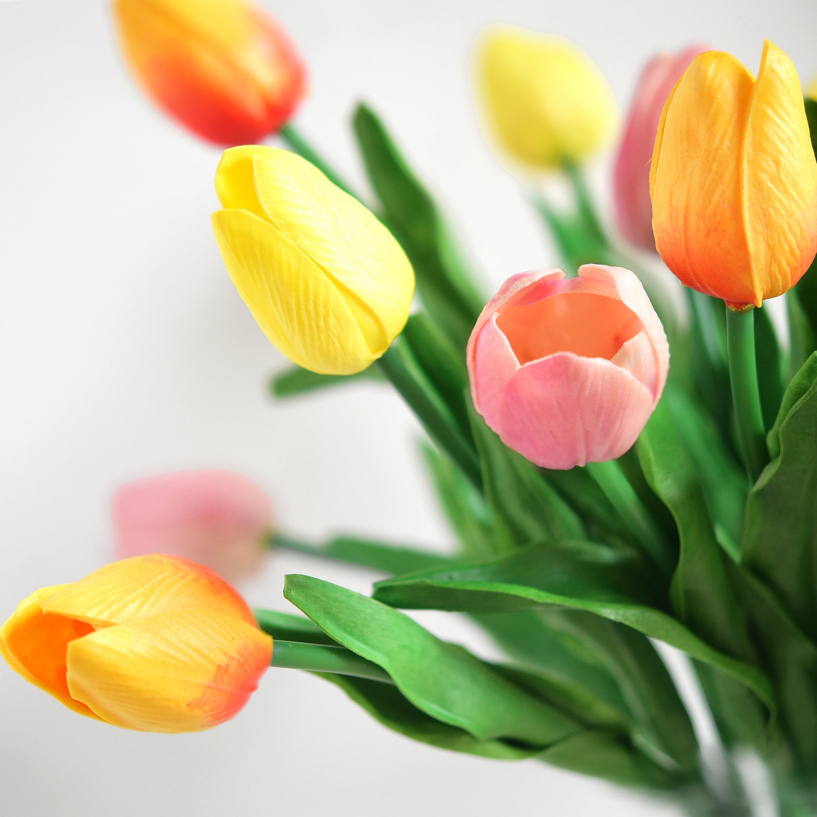 Close-up of artificial tulips with realistic textures and lifelike colors in a glass vase, perfect for home or event décor.
