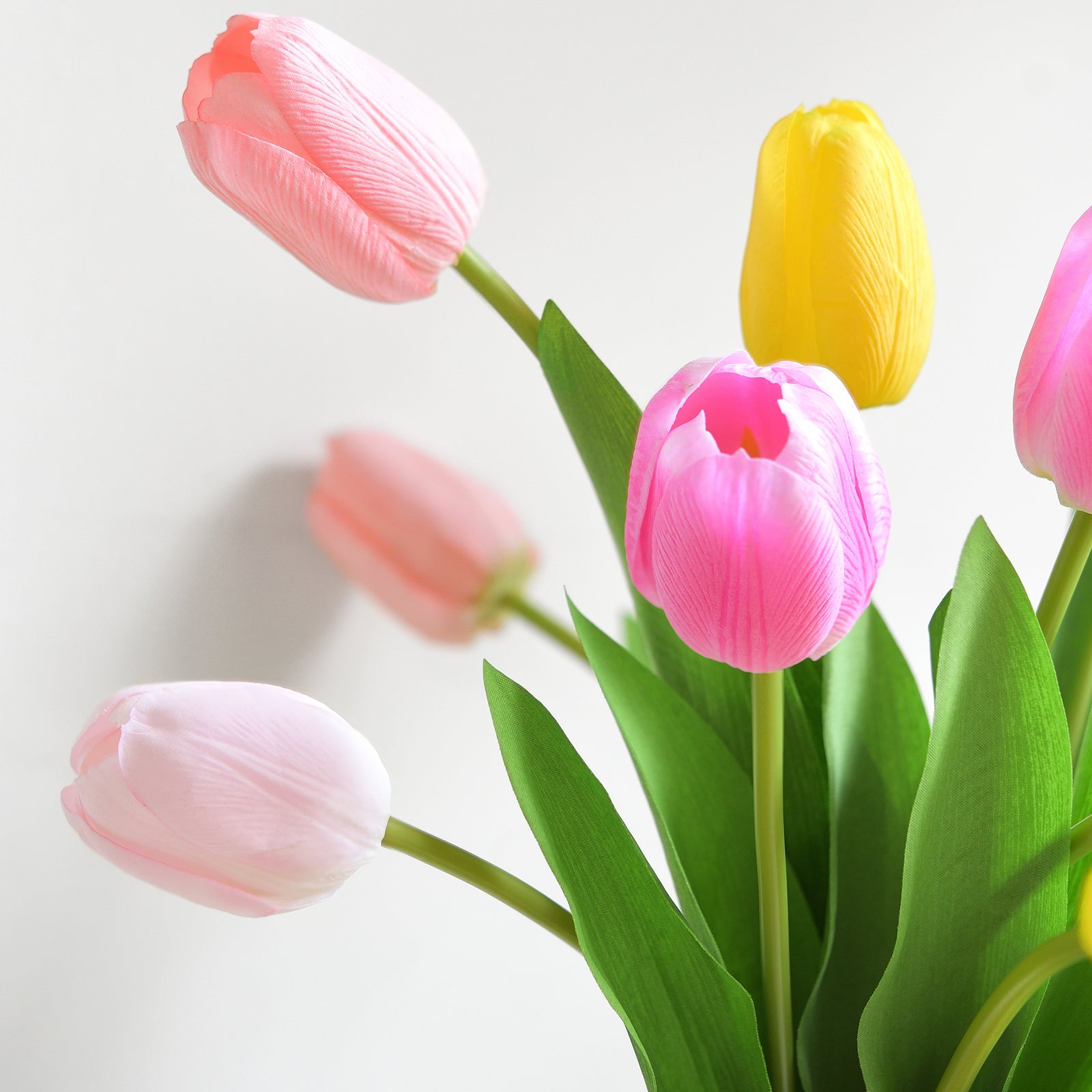 Close-up of artificial tulips in warm orange, pink, and yellow hues with realistic petals and green stems.
