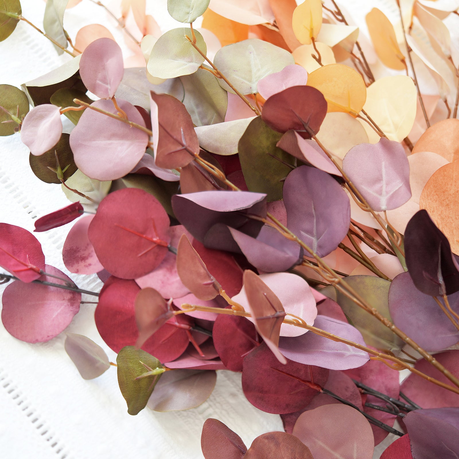 Close-up of handpicked silk eucalyptus leaves in Dusky Ember, Burgundy, and Warm Taupe, highlighting the lifelike colors and textures.