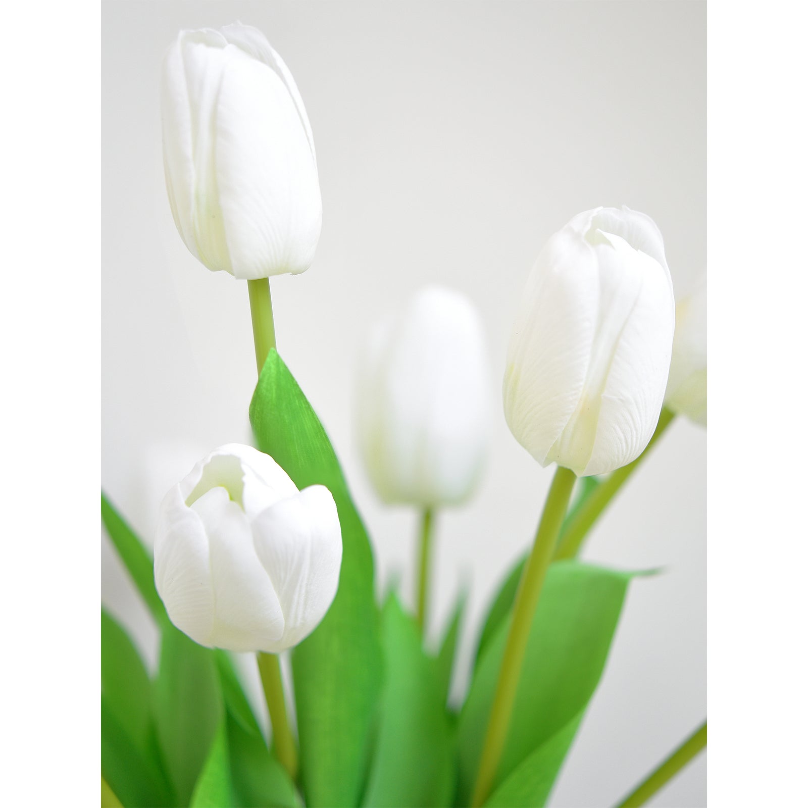 Close-up of realistic artificial white tulip blooms with green leaves, showcasing their lifelike texture and vibrant design.