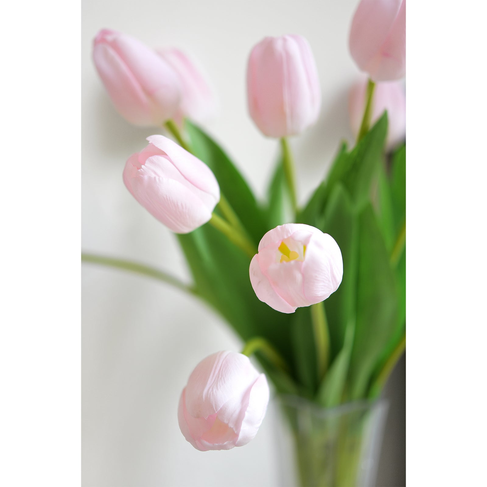 Close-up of soft pink artificial tulips with natural-looking green stems and leaves