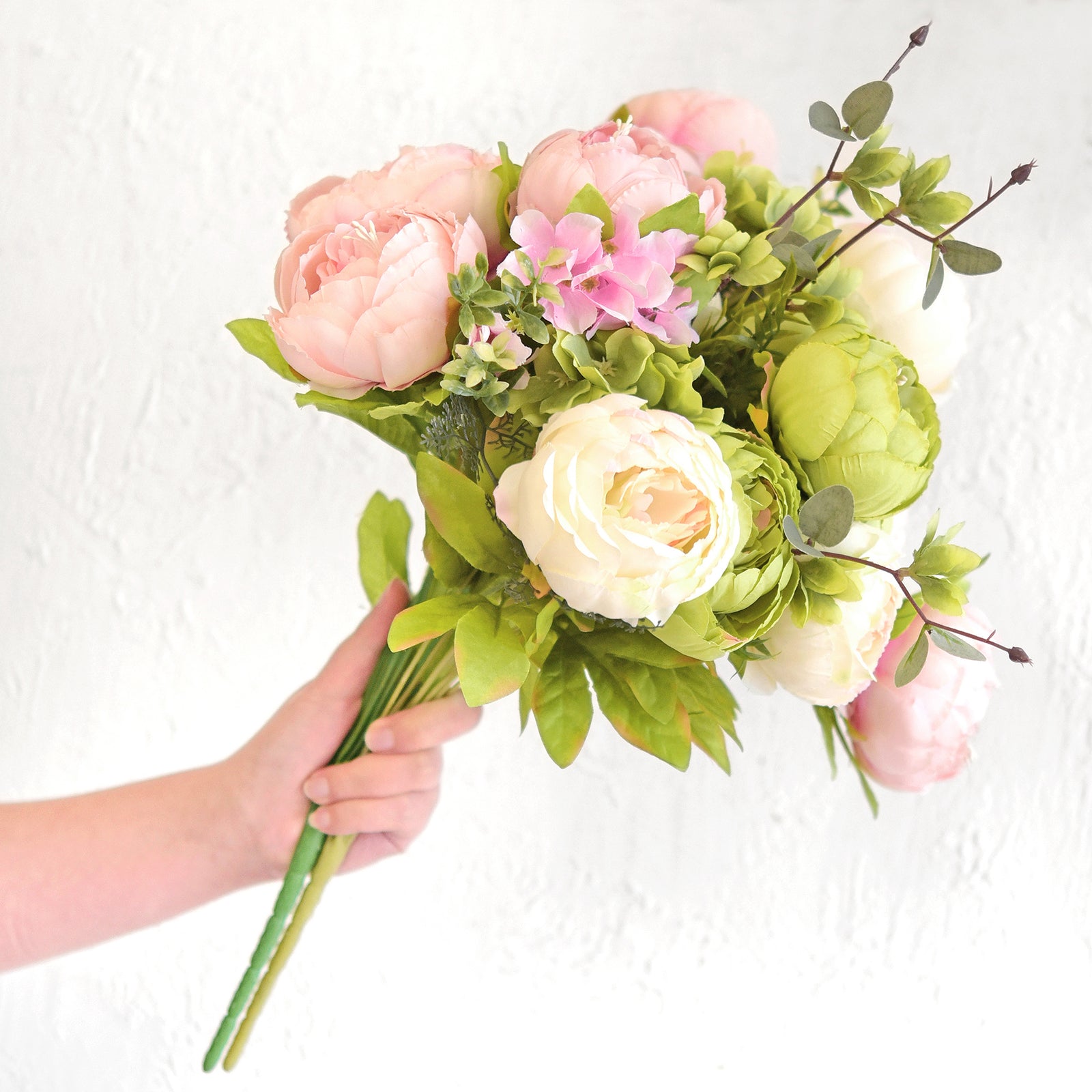 Hand holding a bouquet of artificial peonies and hydrangeas, showcasing flexible stems and lifelike blooms for versatile floral decor.