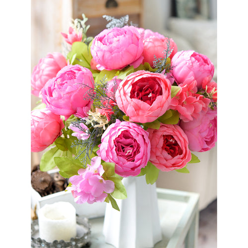 Bright pink silk peonies in a tall white vase, styled with candles and accessories on a modern white tabletop for elegant home decor.