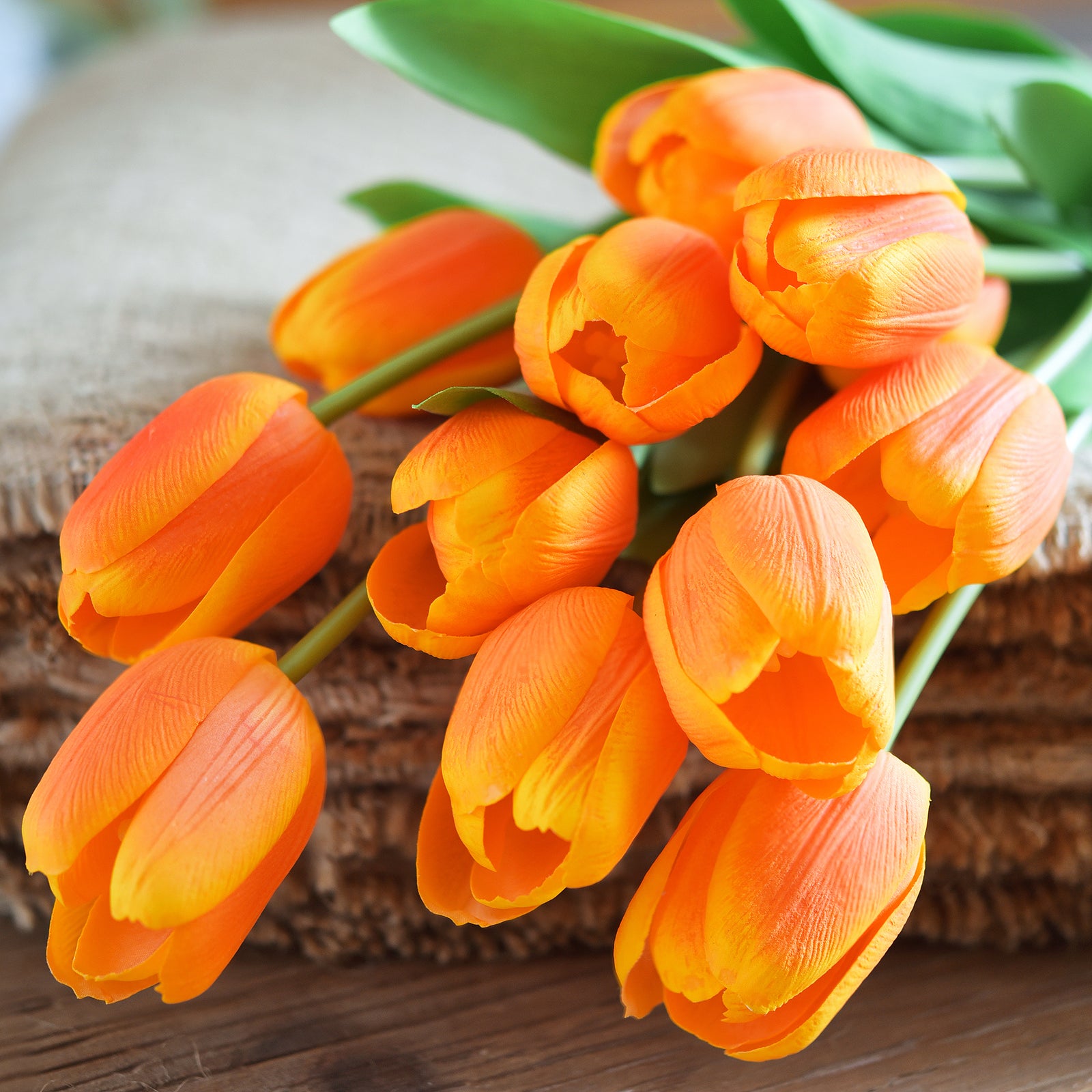 Close-up of vibrant orange artificial tulip bouquet with realistic green leaves.
