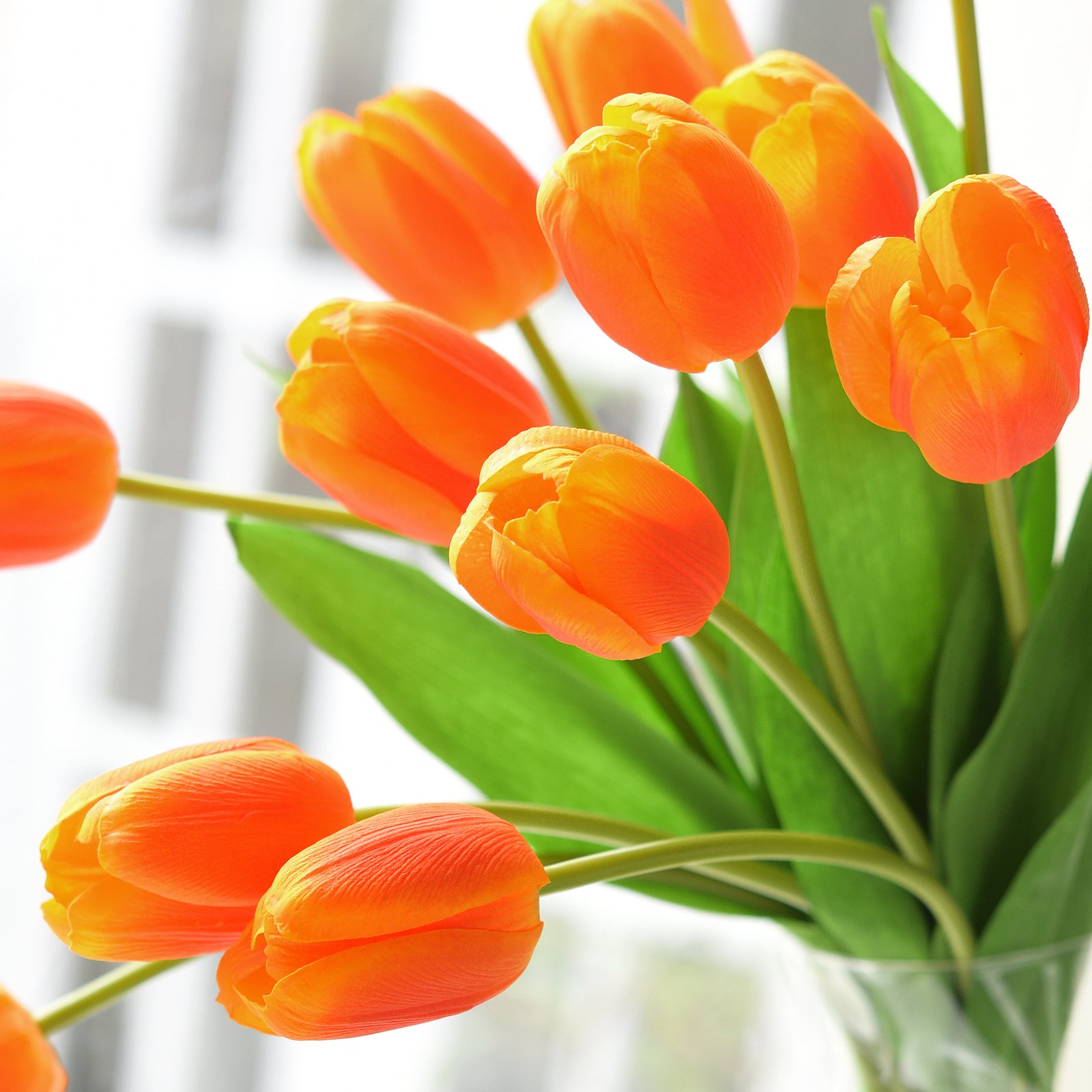 Close-up of vibrant orange artificial tulip bouquet with realistic green leaves