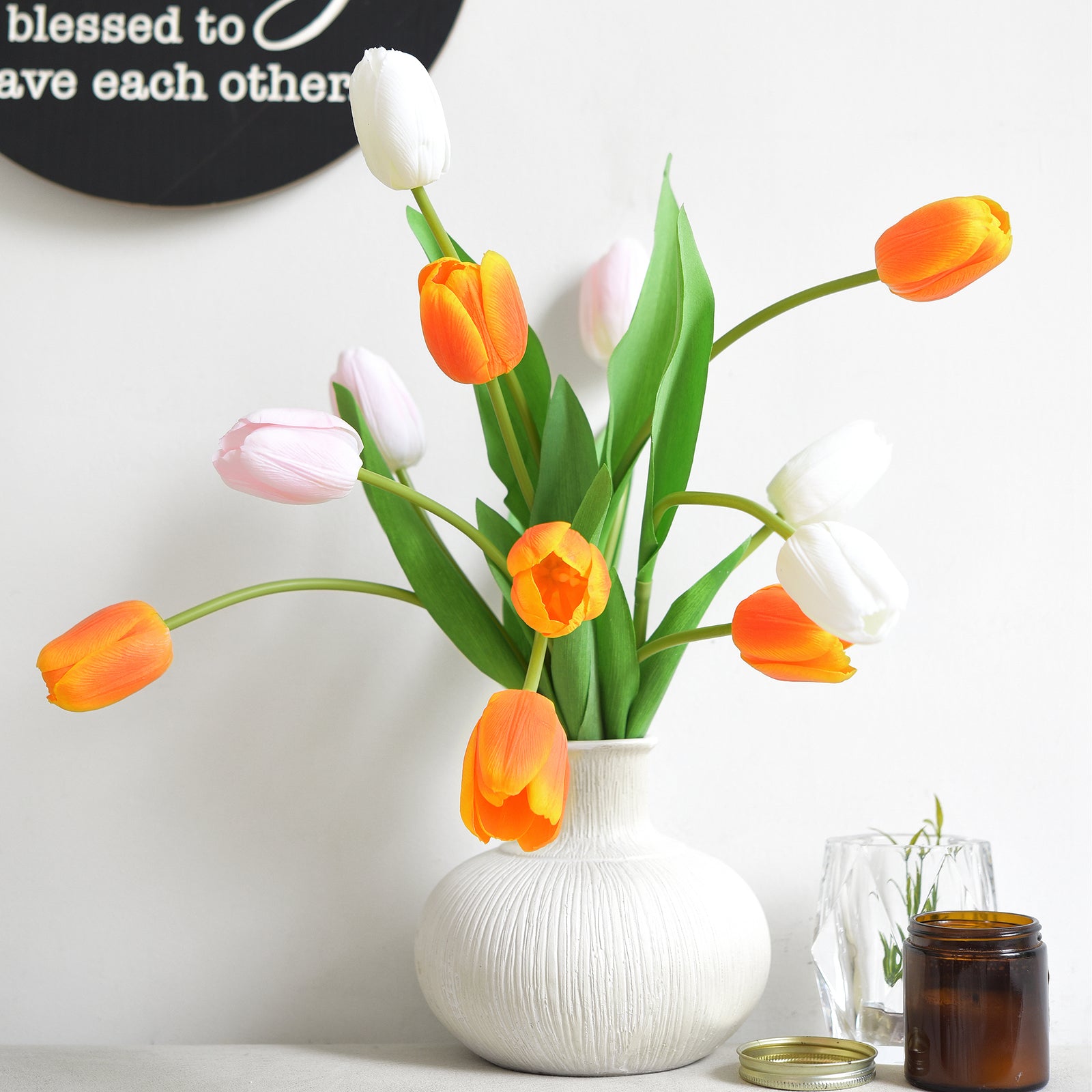 Vibrant orange tulips arranged with a spring bloom mix in a textured ceramic vase.