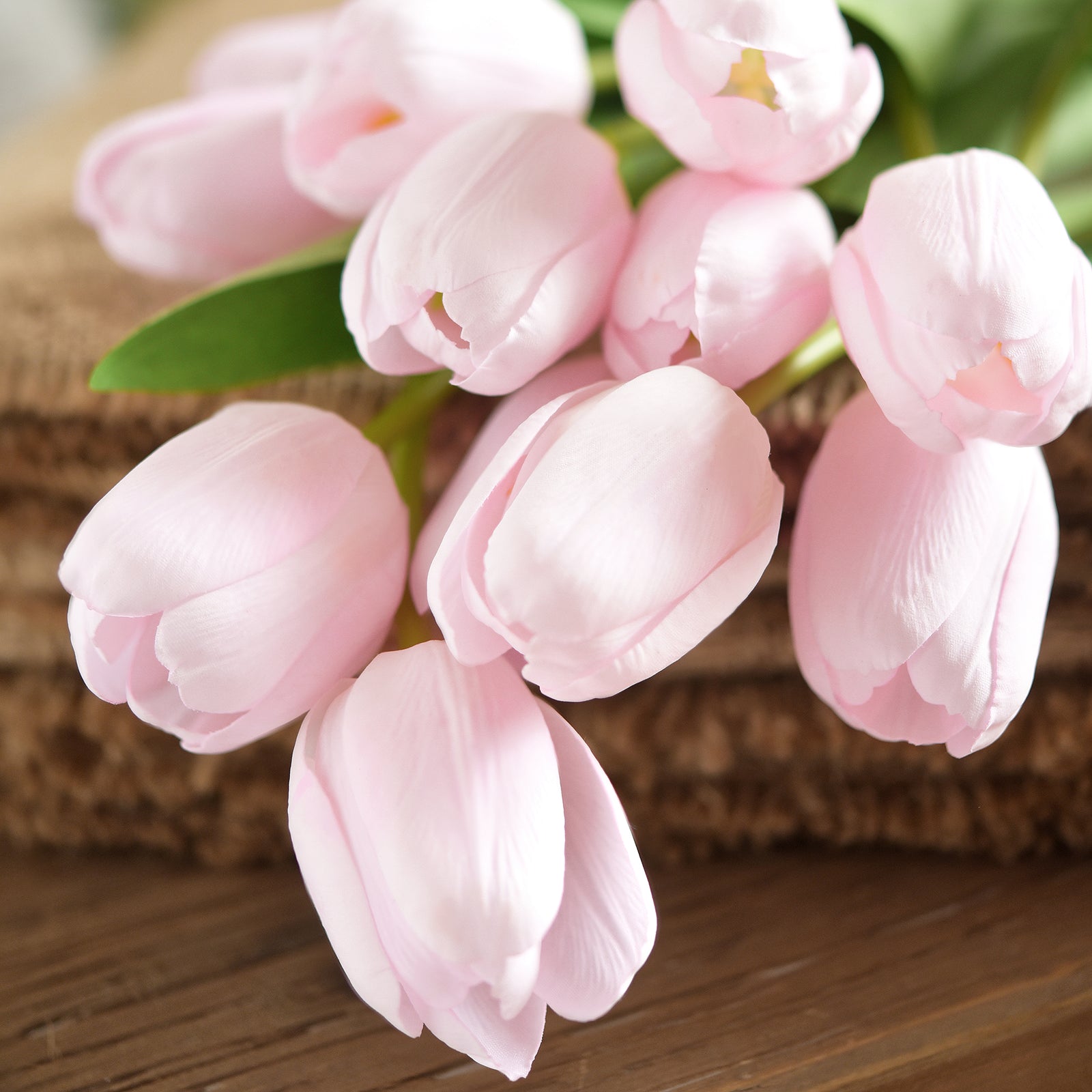 Realistic artificial tulips with pale pink petals displayed on a rustic wooden surface for a classic floral aesthetic.