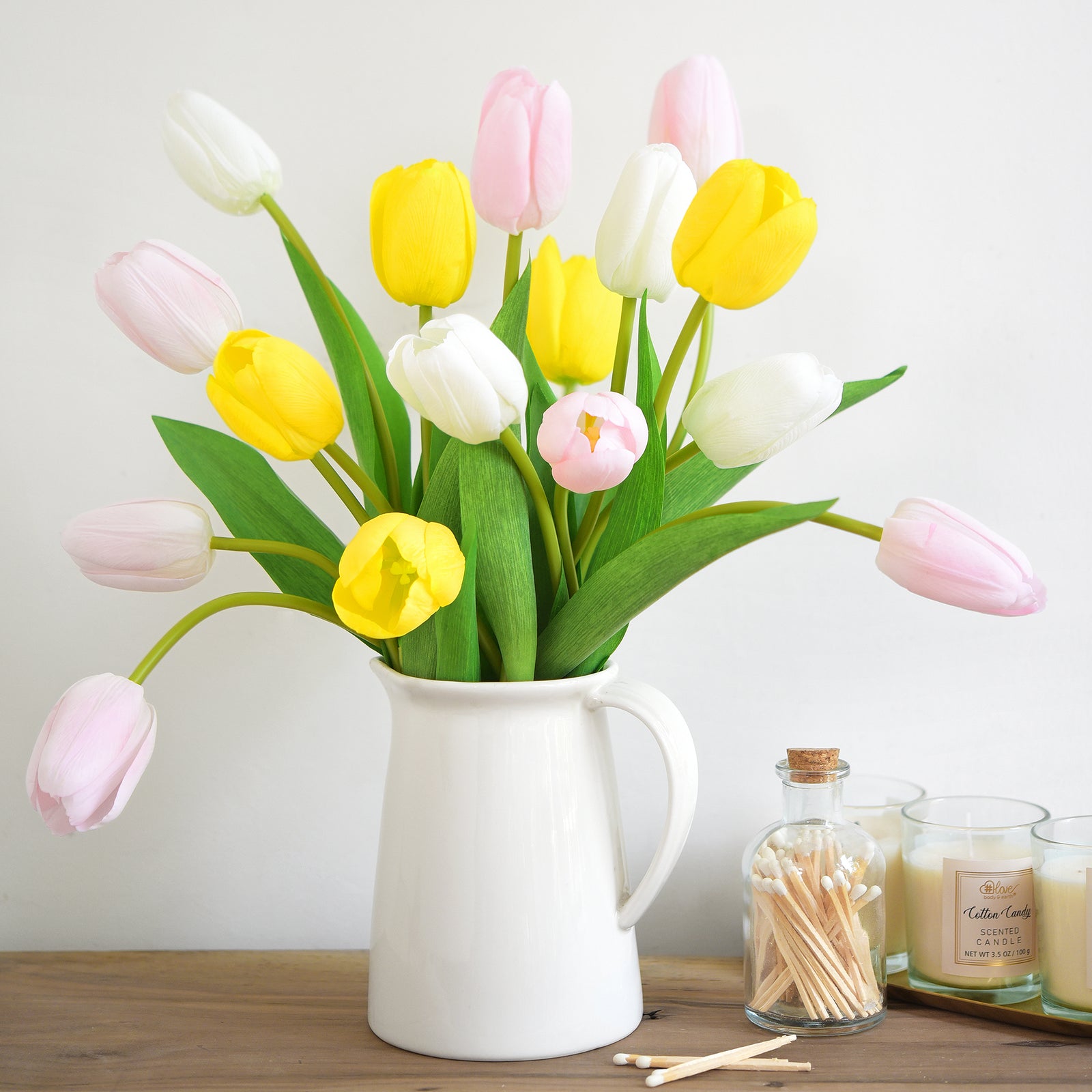 Elegant light pink tulips in a bouquet mixed with white and yellow tulips, arranged in a rustic white pitcher vase.