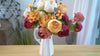 A vibrant mixed peony bouquet featuring cream, burgundy, peach, and pink flowers displayed in a white vase, shown in a video preview.