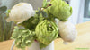 Video for a small arrangement of artificial green and cream peonies in a white vase on a table, showcasing the soft floral petals and leaves.