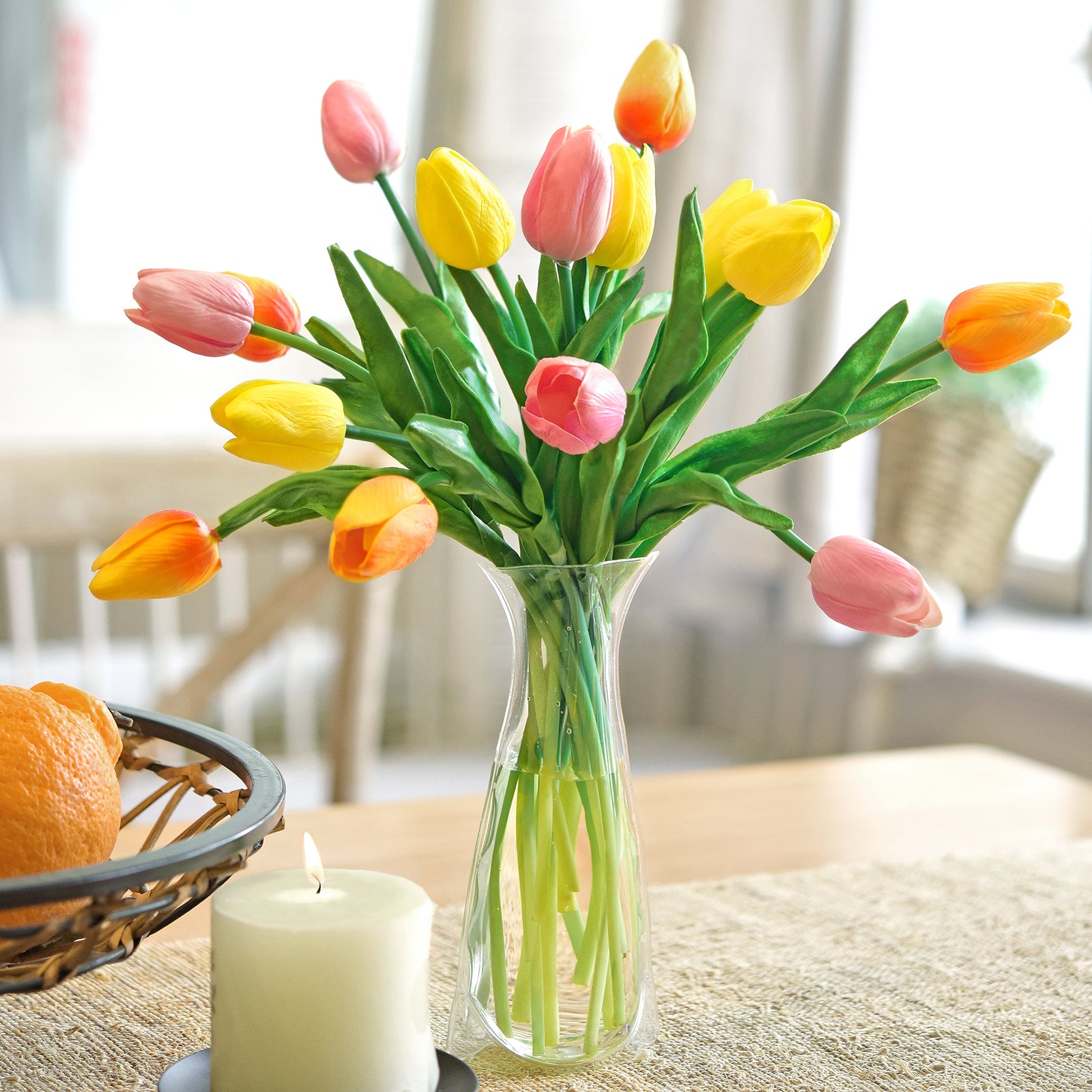 A vibrant bouquet of real-touch tulips in orange, yellow, and pink, displayed in a clear vase on a dining table, adding cheerful spring décor to the space.
