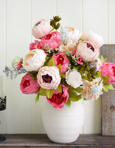 Lifelike silk peony arrangement in a white vase, styled with coral and cream blooms on a rustic wooden shelf for cozy home decor.