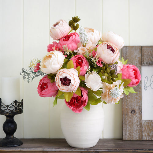 Lifelike silk peony arrangement in a white vase, styled with coral and cream blooms on a rustic wooden shelf for cozy home decor.