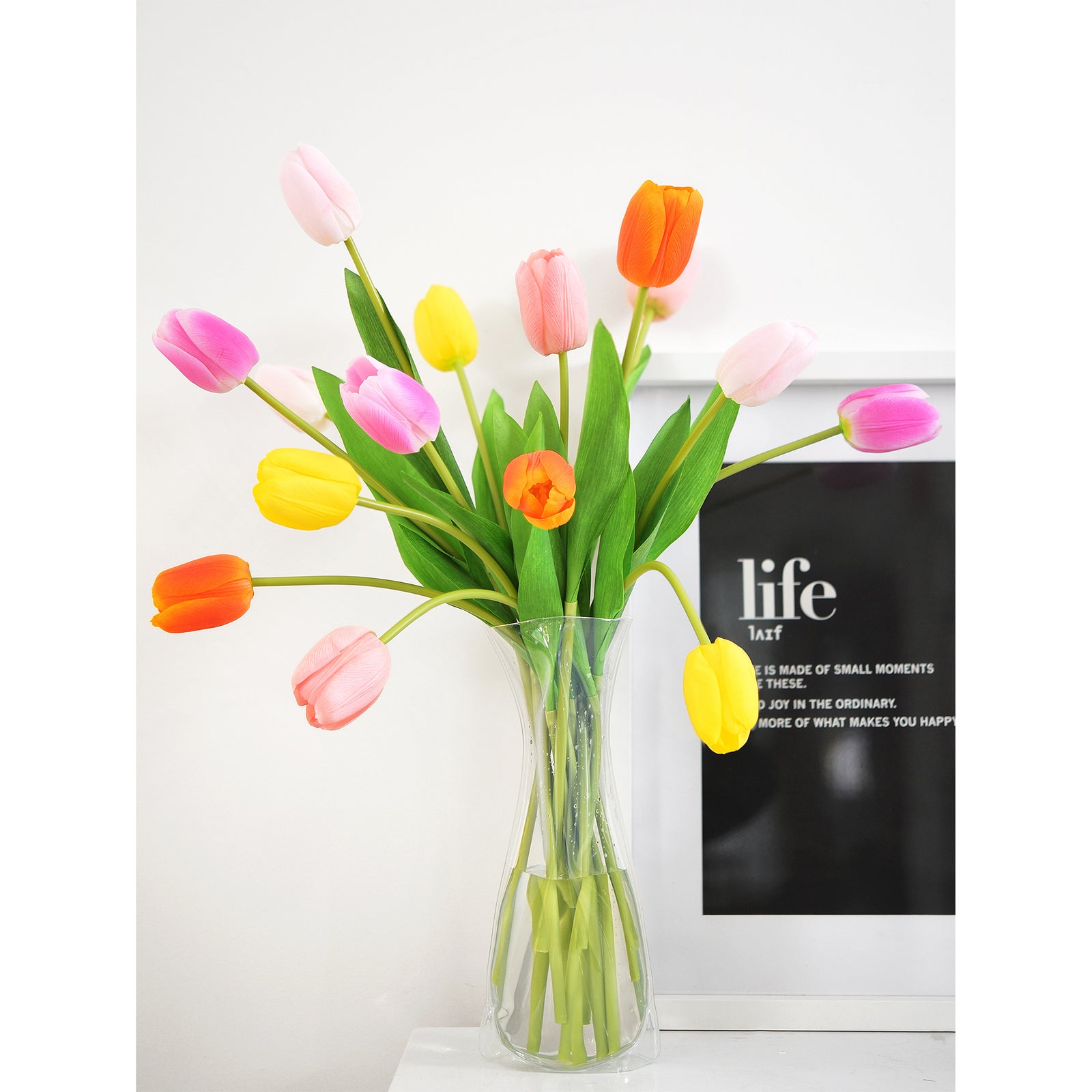 Vivid artificial tulips in orange, yellow, light pink, and hot pink arranged in a clear vase, perfect for modern home decor.
