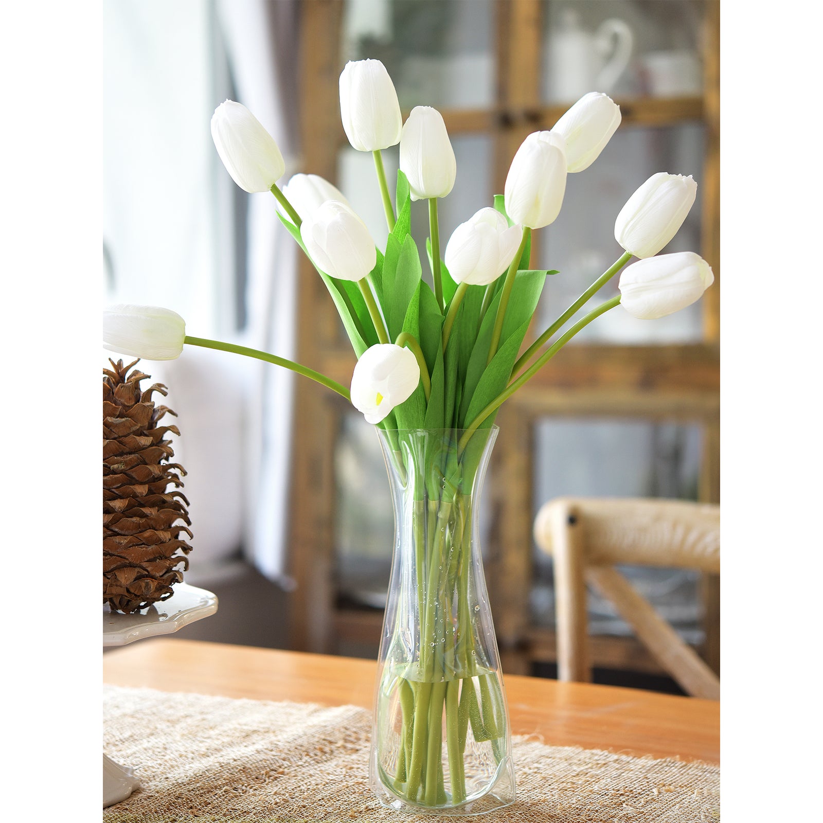 Elegant white artificial tulip bouquet in a clear glass vase, adding a modern touch to a wooden dining table.