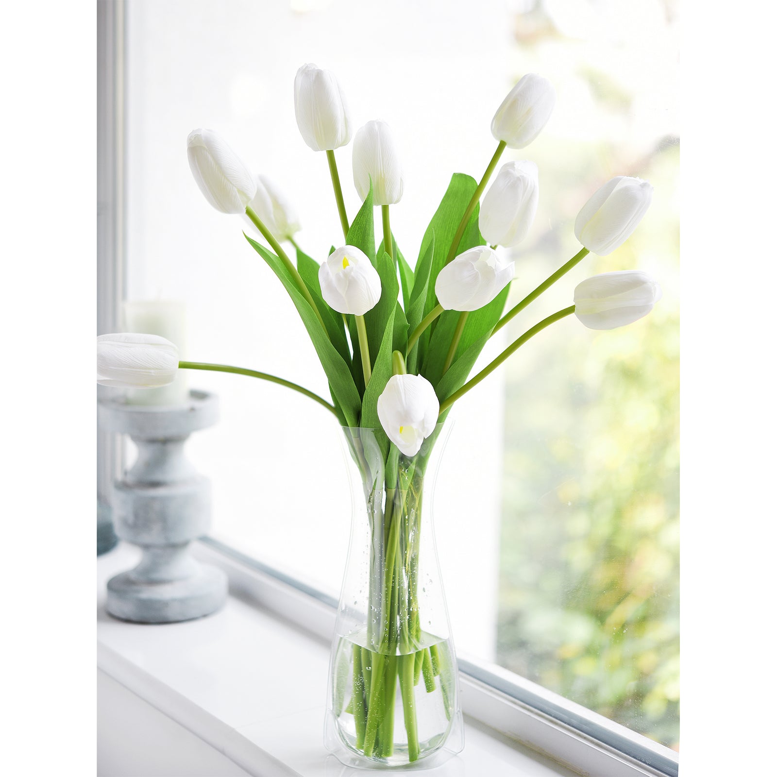 Artificial white tulip arrangement in a glass vase placed near a window, creating a serene and minimalist ambiance