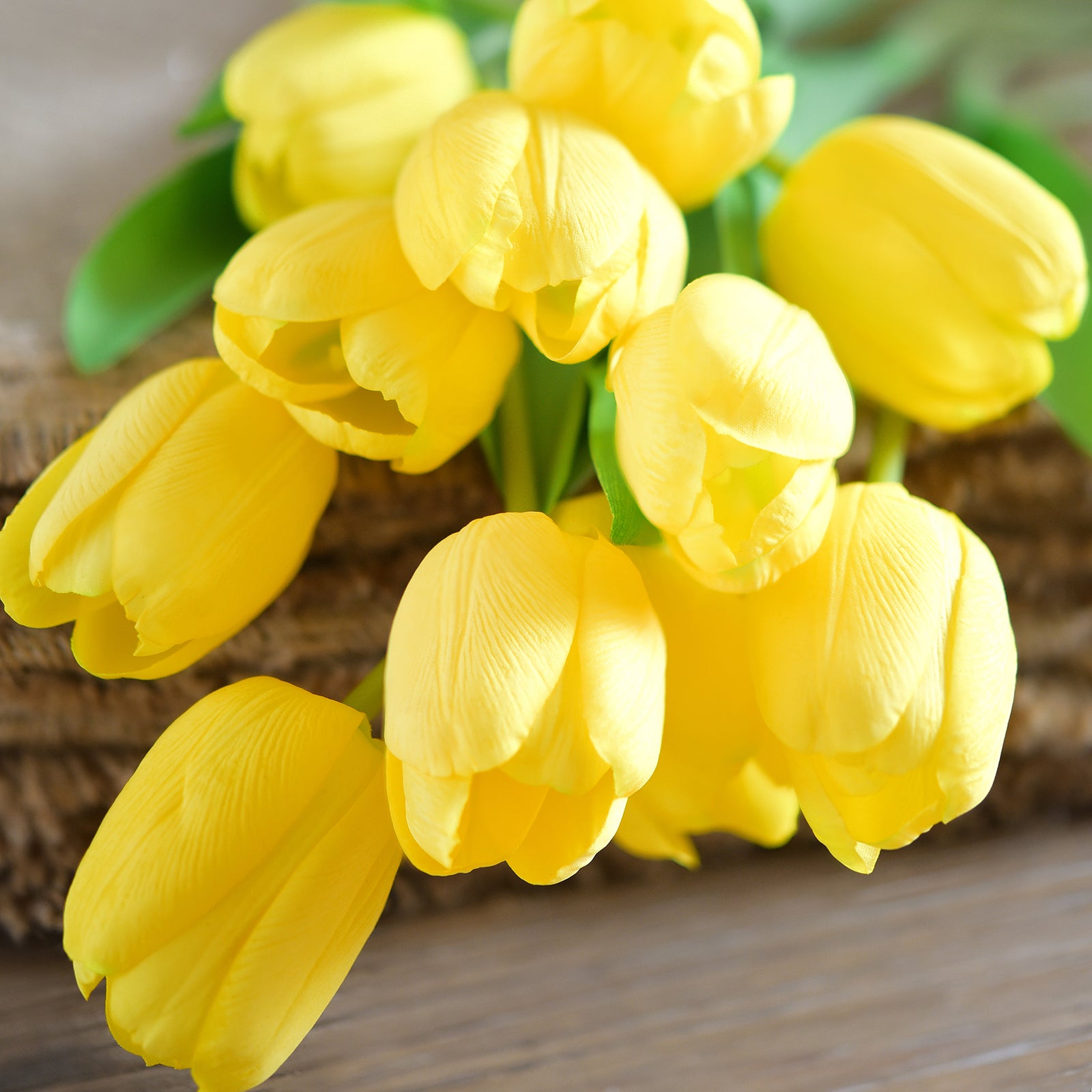 Bunch of artificial yellow tulips arranged on a rustic wooden surface.