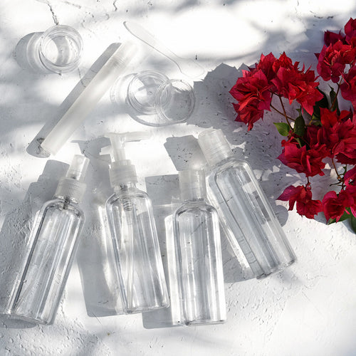 Transparent travel bottles displayed outdoors with red flowers and sunlight

